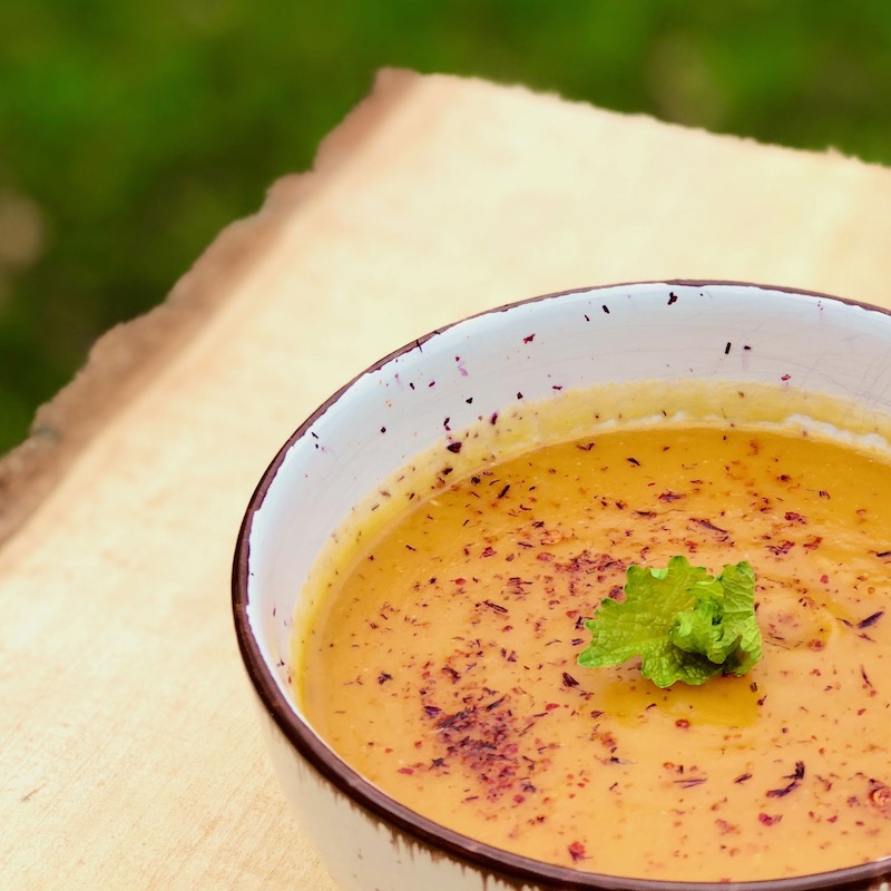 Rezept für Süßkartoffelsuppe mit roten Linsen und Harissa vegan das Bild zeigt die Suppe in einer Bowl auf einem Holzbrett mit Topping