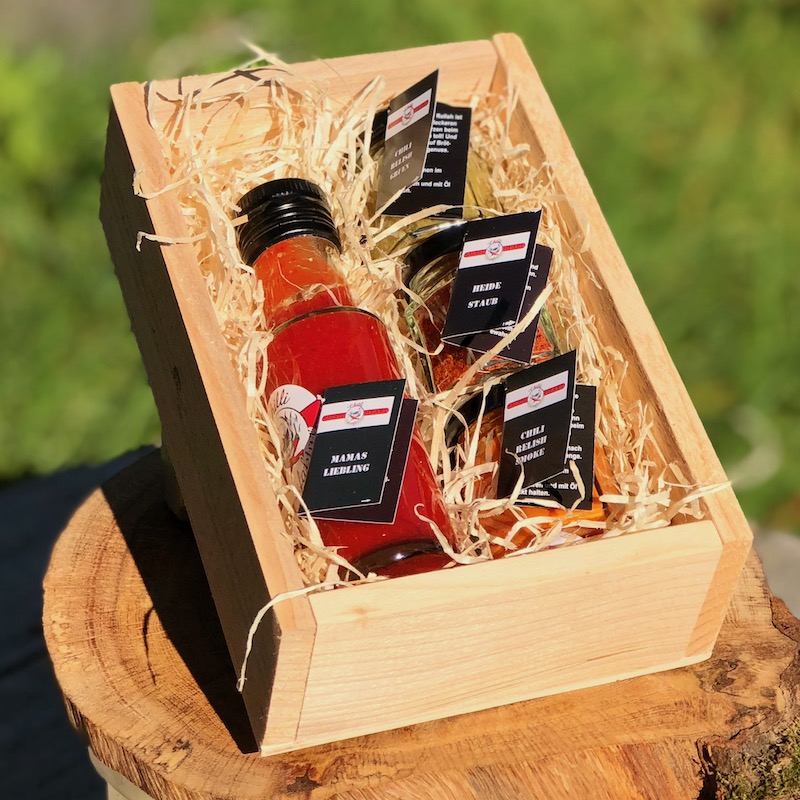 Das Bild zeigt die Chili Geschenkbox Feuer und Flamme der Inhalt ist die Sauce Mamas Liebling, Chili Relish smoke Heidestaub und Chili Relish grün