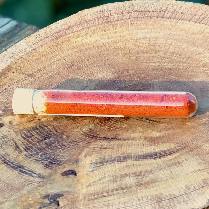 Chili Pulver Schärfegrad 5 kaufen Das Bild zeigt ein Glasröhrchen mit Chili Pulver "Schärfegrad 5"zum Kaufen auf einer Holzscheibe liegend