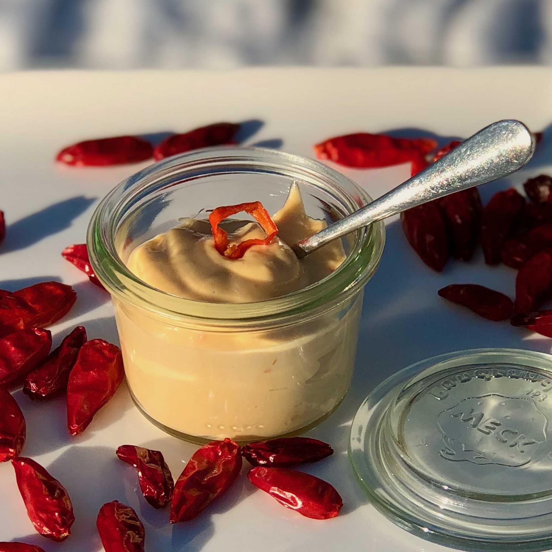 Chili Mayonaise im Glas auf einem Teller stehend  mit Chilischoten dekoriert