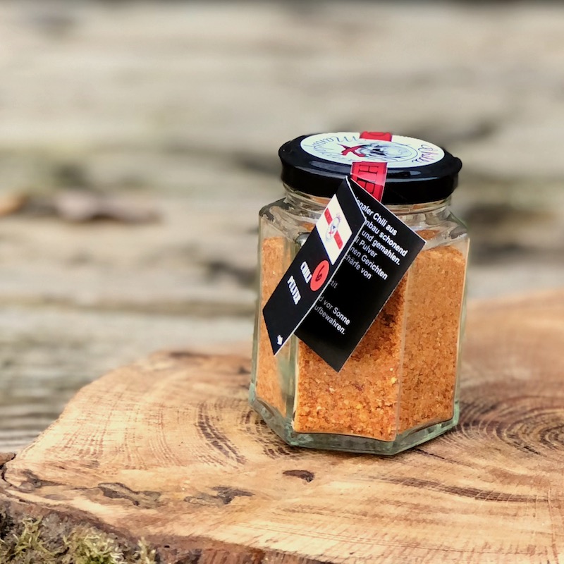 Chilipulver Schärfegrad 6 kaufen Chilipulver Schärfegrad im Glas von der Chilli Manufaktur auf einer Holzscheibe auf einem Tisch stehend zum kaufen