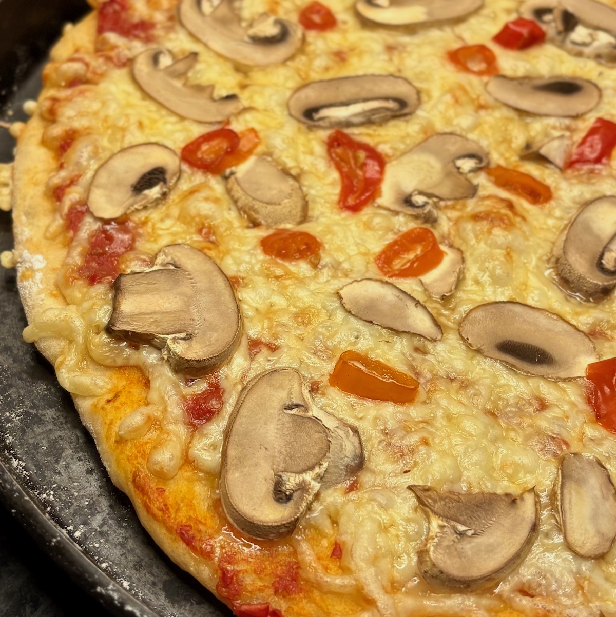 Pizza mit Pizza Chili und Pilzen belegt auf einem Pizzablech als Rezeptvorschlag