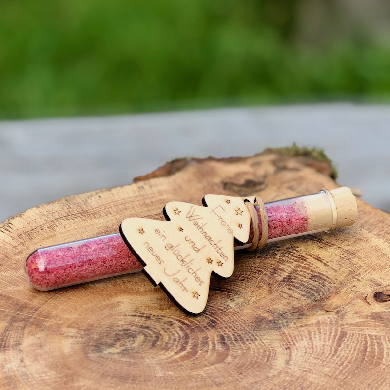 Giveaway frohe Weihnachten & ein glückliches neues Jahr kaufen Glasröhrchen mit Blütensalz und Holzanhänger mit dem Aufdruck "frohe Weihnachten und ein glückliches neues Jahr" auf einem Tisch liegend mit Lichterkette und Strohstern