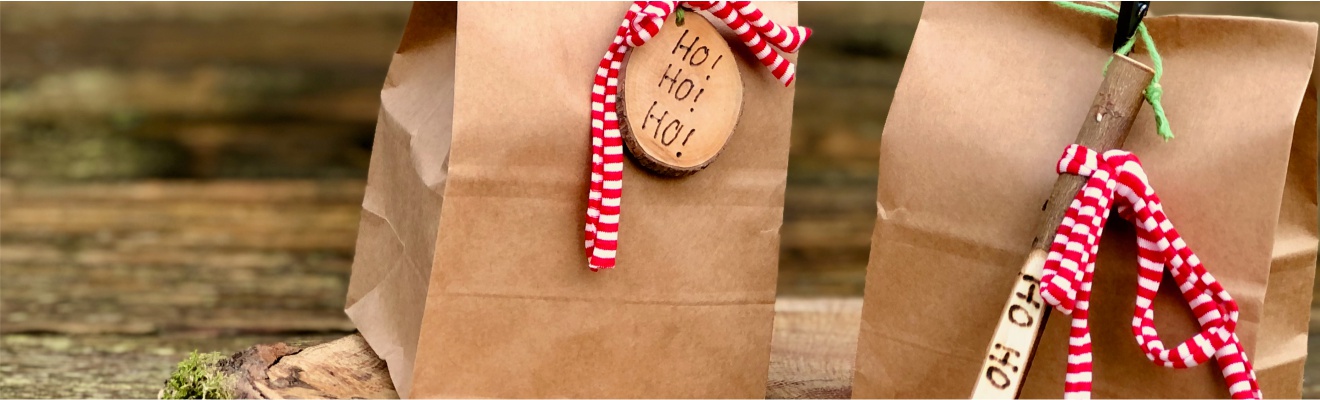 Nikolaus Geschenk - zwei Geschenktüten zum Nikolaus aus Papier mit Ho Ho Ho Anhänger und rot-weißer Schleife auf einem Tisch stehend