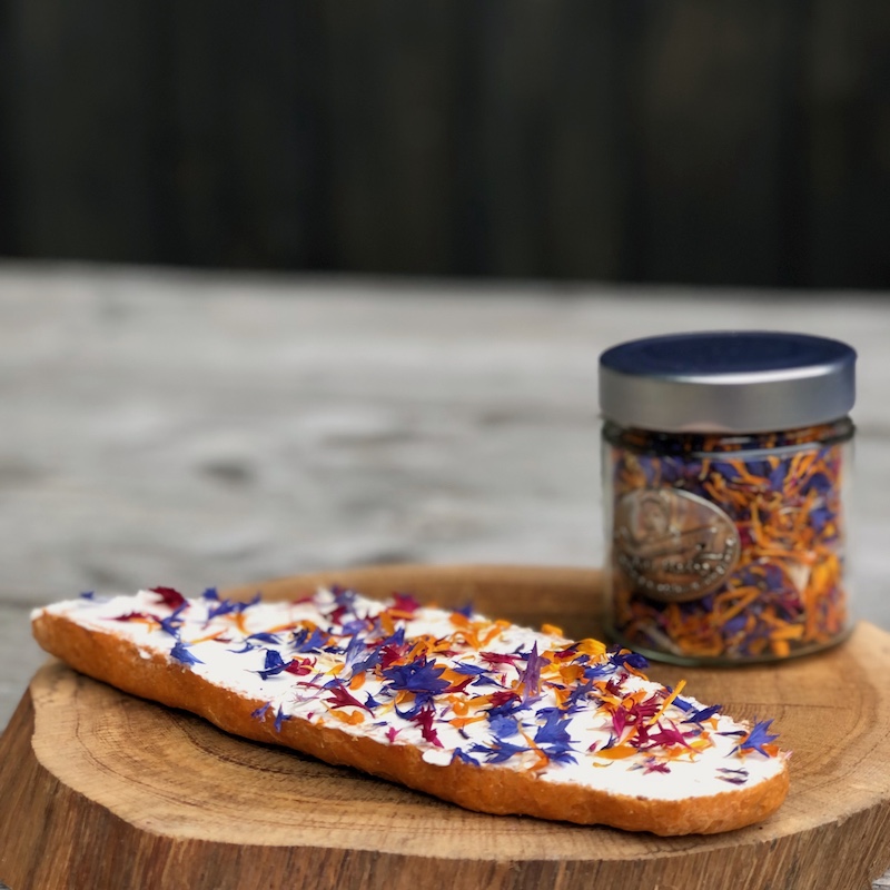 essbare Blüten auf einem Brot mit Frischkäse auf einem Holzteller als Serviervorschlag