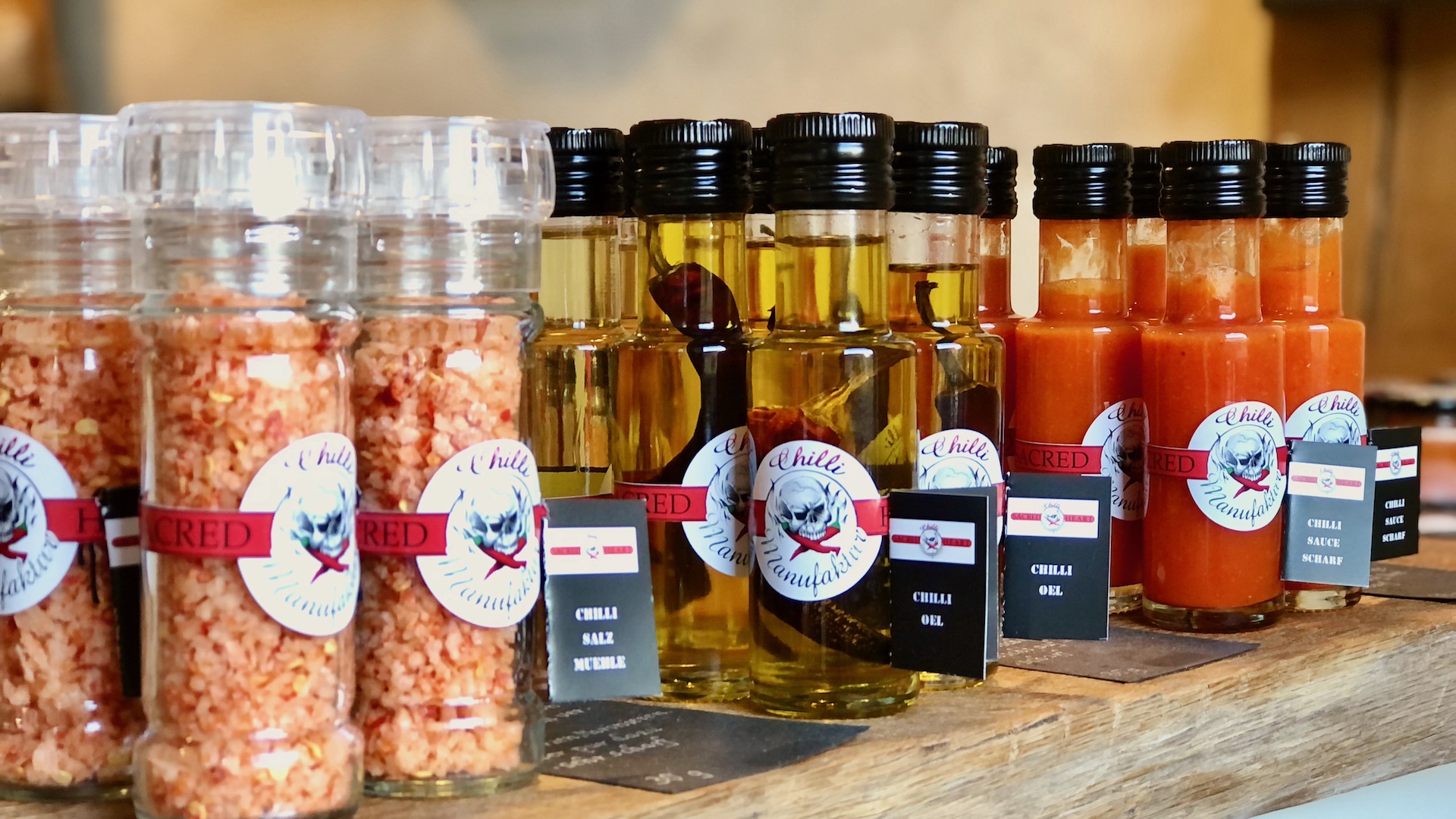 Das Bild zeigt Chili Salzmühlen, Chiliölflaschen und Chilisaucen in der Flasche auf einem Eichentisch im Hofladen stehend Chilli Manufaktur Susanne Menke Lüneburger