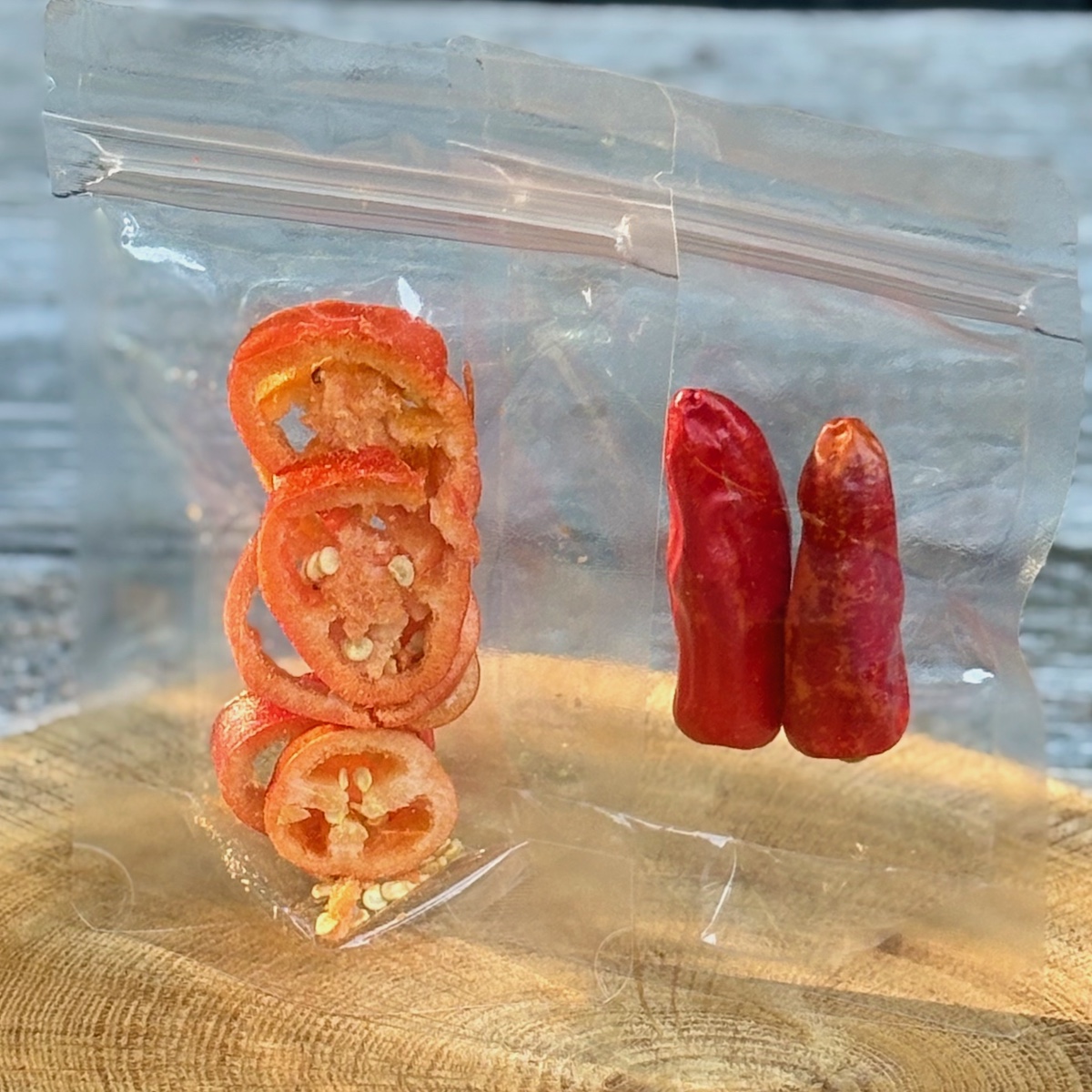 Freeze dried Chili in zwei Sorten: geschnittene Scheiben oder ganze rote Schoten im Standbodenbeutel Klarsicht auf einer Holzscheibe ist inhalt vom Chili Probierset Heide Crunch Chili