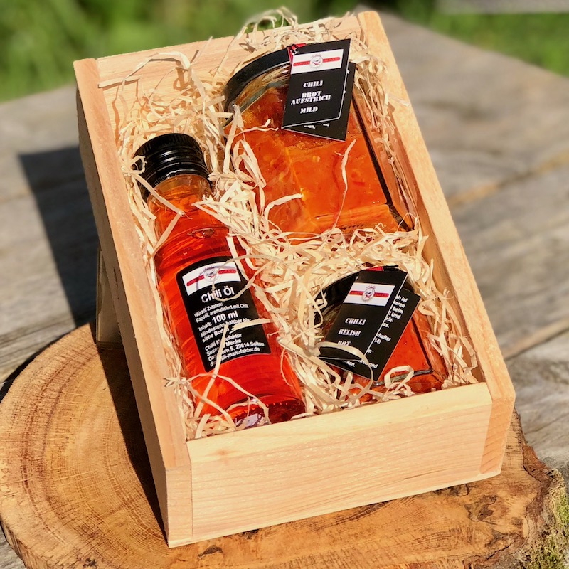Kulinarische Chili Geschenkbox feuriger Start. Es ist eine Holzbox mit dem inhalt Chili Brotaufstrich mild, chiliöl und Chili Relish rot