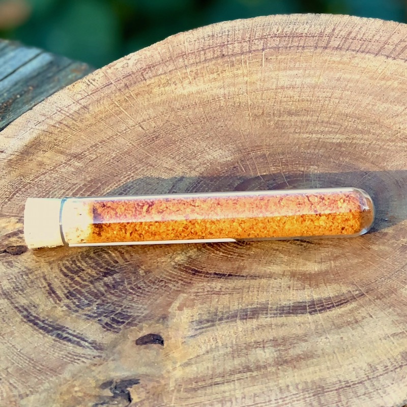 Chili Pulver Schärfegrad 6 kaufen Das Bild zeigt ein Glasröhrchen mit Chili Pulver "Schärfegrad 6" zum Kaufen auf einer Holzscheibe liegend