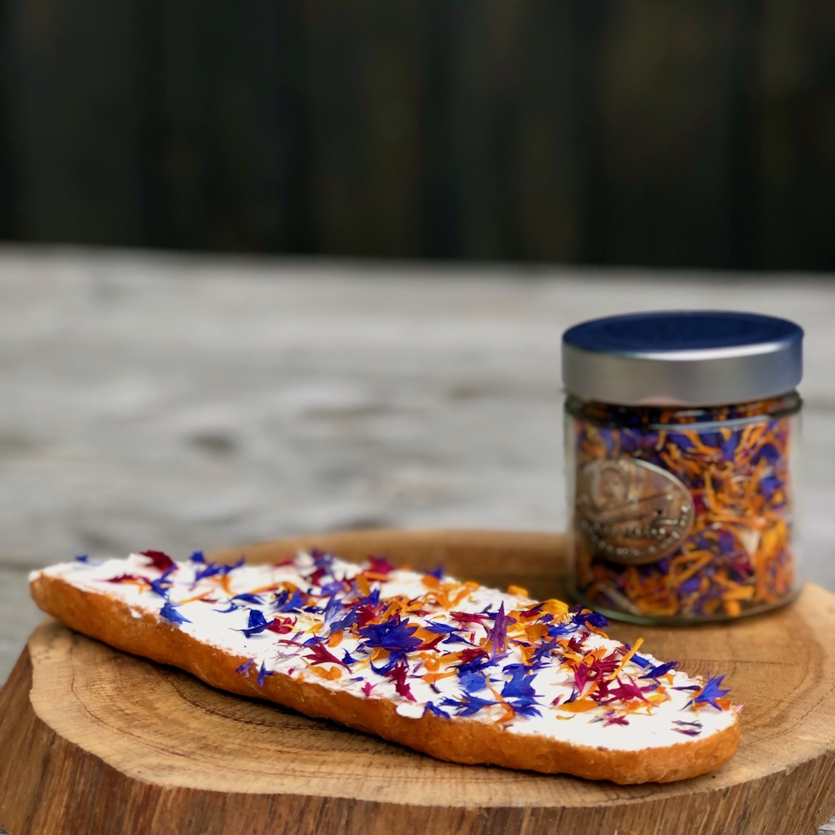 Essbare Blüten "Butterblüten" auf einem Brot mit Frischkäse gestreut liegend auf einem Holzteller