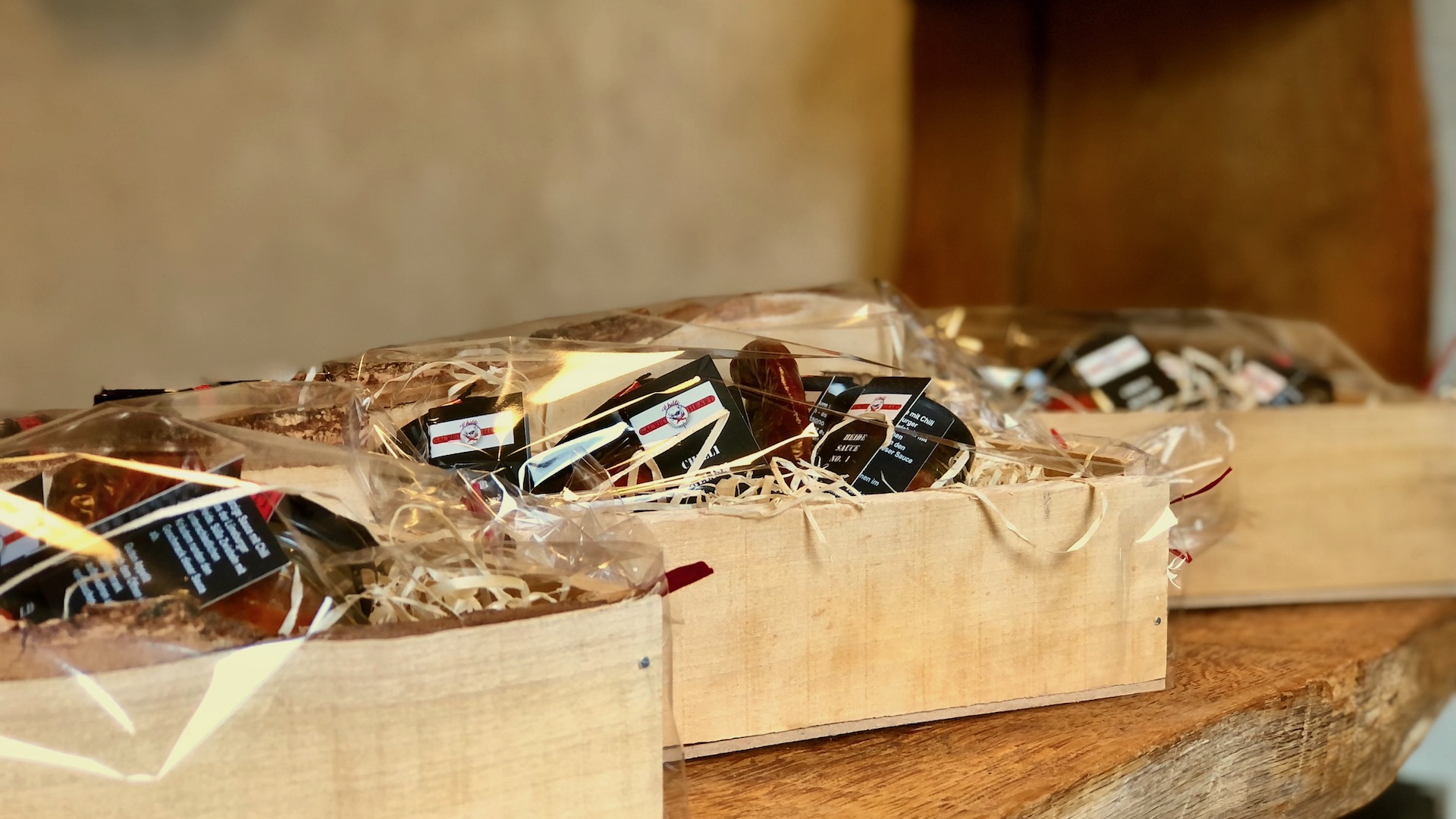 Das Bild zeigt drei exklusive Geschenkboxen aus Birkenholz mit unterschiedlichen Chiliprodukten auf einem Eichentisch im Hofladen Chilli Manufaktur Susanne Menke Lüneburger Heide