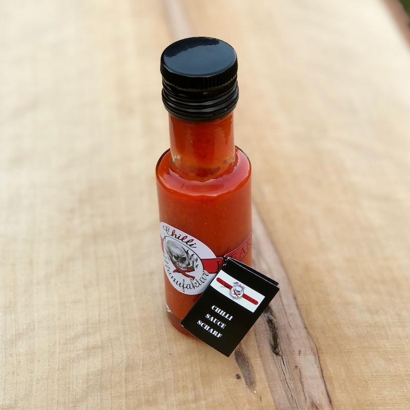 Das Bild zeigt eine Flasche mit Scharfe Chili Sauce in rot auf einem  Holztisch von der Chilli Manufaktur zum Kaufen