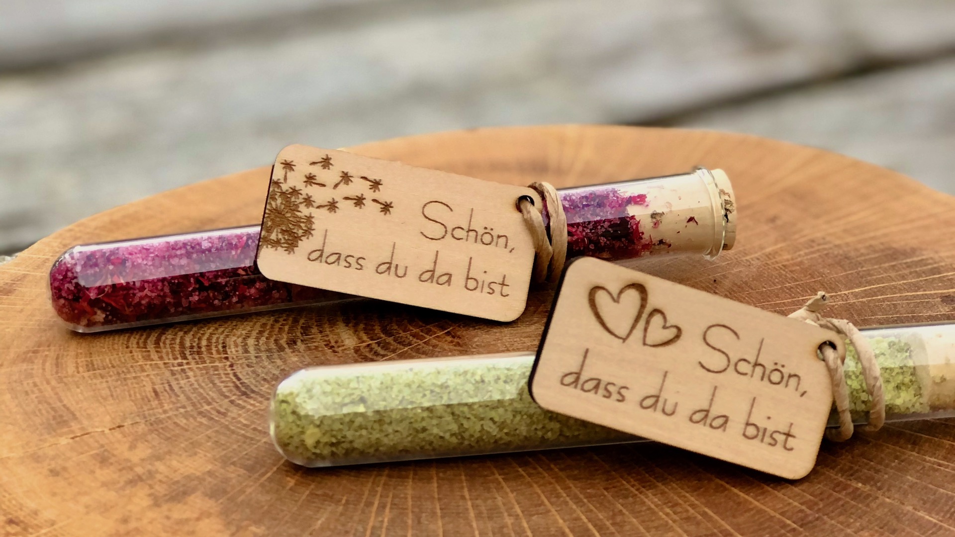 Das Bild zeigt zwei Gastgeschenke mit Salz im Reagenzglas und Anhänger aus Holz mit der Beschriftung Schön, dass du da bist als Gastgeschenk für Teammeeting Geburtstag Familienfeier