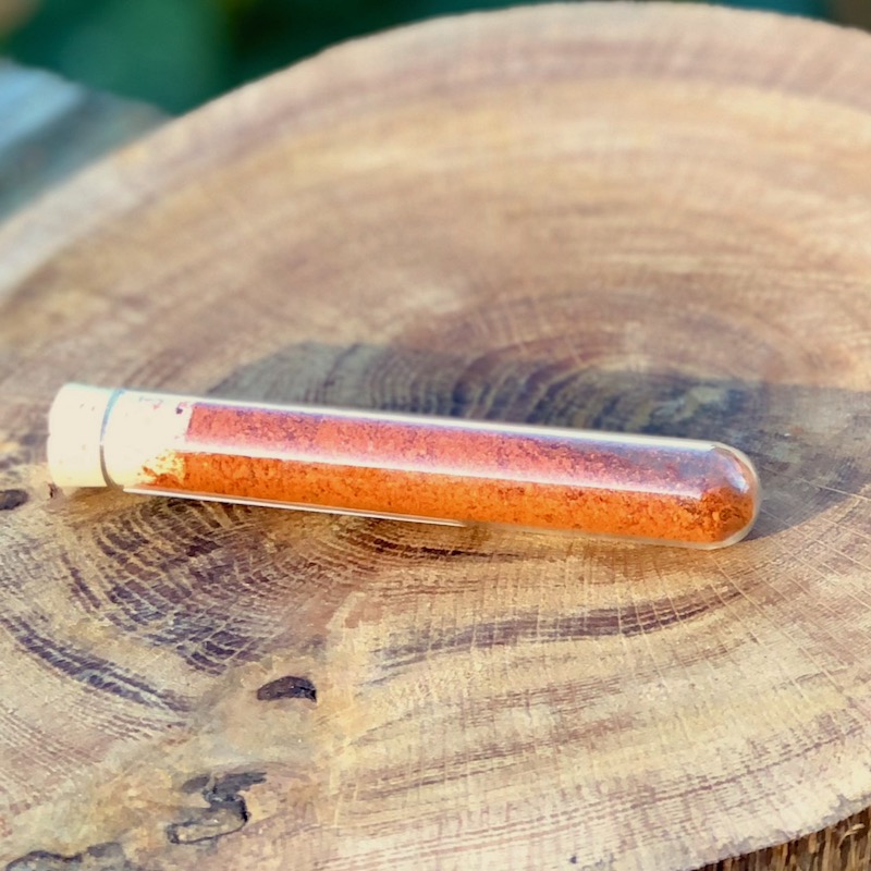 Chili Pulver Schärfegrad 7 kaufen Das Bild zeigt ein Glasröhrchen mit Chili Pulver "Schärfegrad 7" zum Kaufen auf einer Holzscheibe liegend